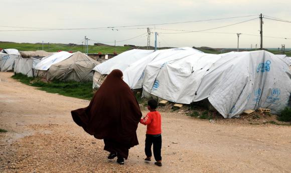 امرأة تمسك بيد طفل صغير وسط مخيم للاجئين