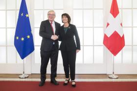 Un hombre y una mujer se dan la mano entre dos banderas, la suiza y la europea.