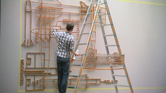 Man installing a wire sculpture on museum wall