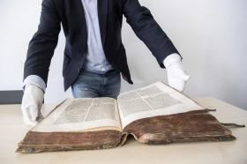 Mann mit weissen Handschuhen präsentiert altes Buch
