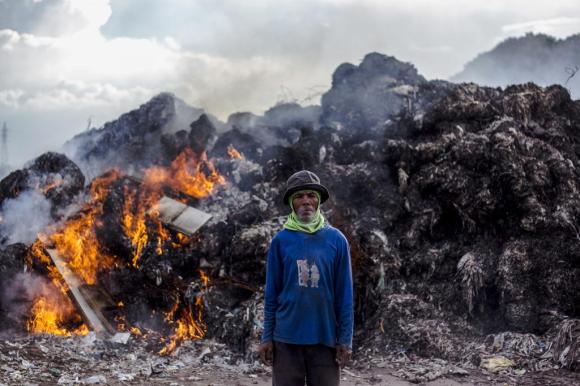 Un hombre frente a montaña de basura que arde.