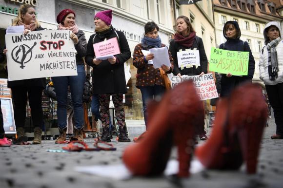 Mujeres con pancartas y, en el suelo, zapatos rojos de tacón alto.