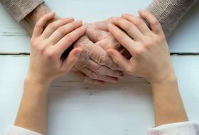 Unas manos de una persona más joven sobre las manos de una persona mayor