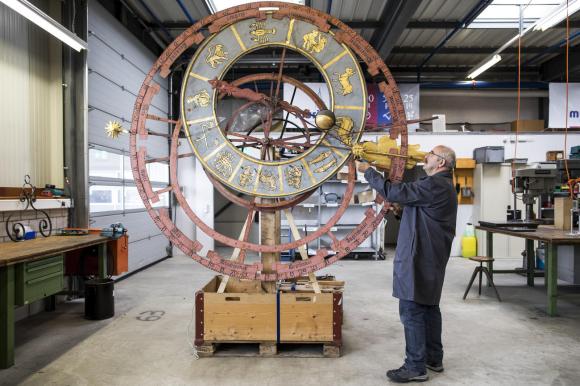大きな時計の文字盤を修理する男性