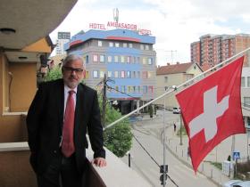 uomo in posa accanto alla bandiera svizzera