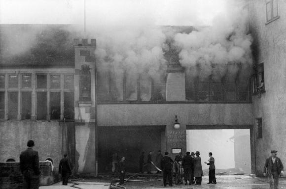 Ein brennendes Gebäude auf einer schwarz-weiss Aufnahme.