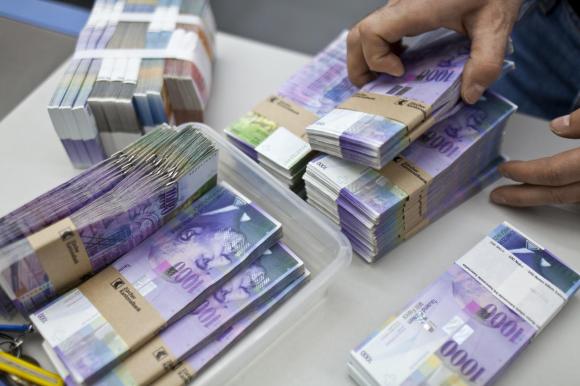 رجل يتعامل مع مجموعة من الأوراق النقدية من فئة ألف فرنك سويسري داخل مصرف في زيورخ