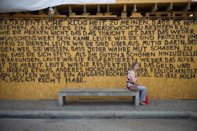 Eine Passantin sitzt auf einer Bank vor einer riesigen Wörterwand.