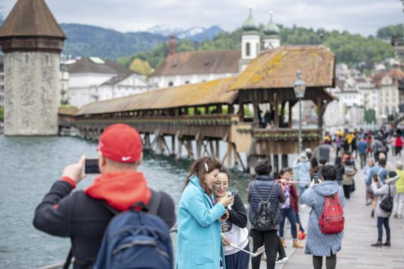 Tourists in Lucerne take photos by the iconic Chapel Bridge
