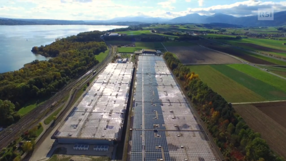 Vista del tetto di un lungo edificio industriale in aperta campagna, con lago sulla sinistra e verde altrove