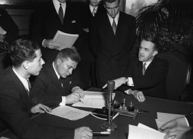 Tre uomini attorno a un tavolo firmano un documento