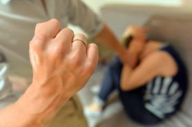 Un hombre levanta un puño para golpear a una mujer enconchada en un sofá (imagen posada)