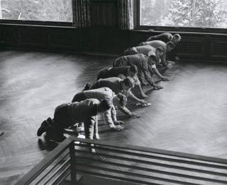 A group of men lined up on their hands and knees, polishing a wooden floor.