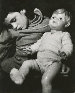 A young child sleeps while holding a doll.