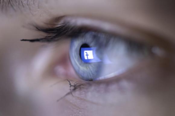 The logo of Facebook is reflected in the eye of an adolescent, photographed in Zuric h