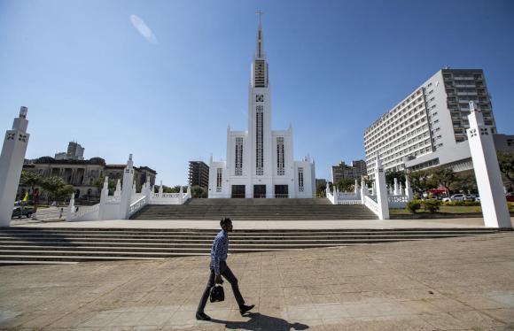 Homem caminha frente a uma igreja em Maputo