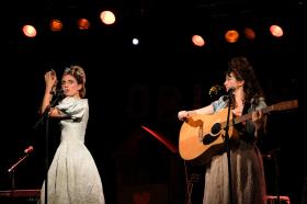 Dos mujeres en un escenario: una toca la guitarra y otra canta