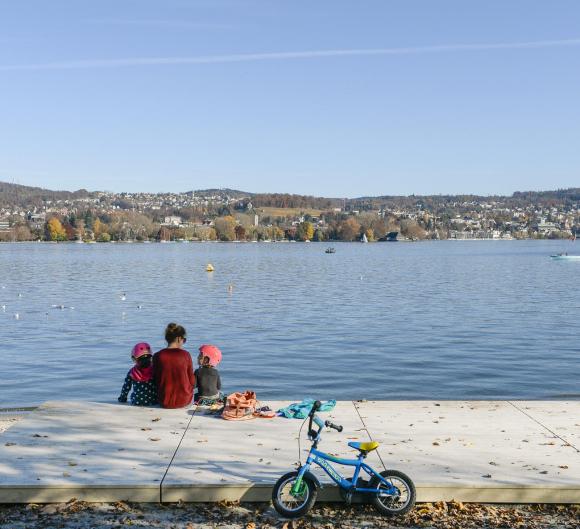 Una mujer y dos niños sentados a orillas de un lago