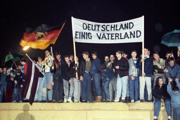 Manifestantes en el Muro de Berlín con una banderola que dice: Alemania, un solo país