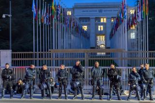 Hombres sentados. encadenados a las rejas del Palacio de Naciones. Ante ellos, uncordón policial