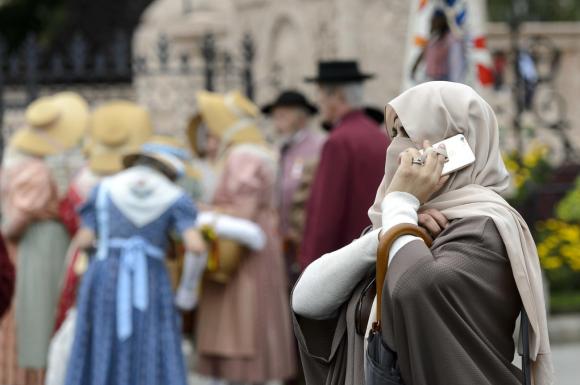 Women with face covering using mobile phone, people in traditional Swiss costumes in background