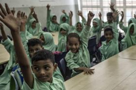 مجموعة من الأطفال اللاجئين يرفعون اصابعهم في فصل دراسي