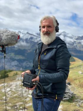 Philip Samartzis con un aparato para grabar, en medio de un paisaje alpino