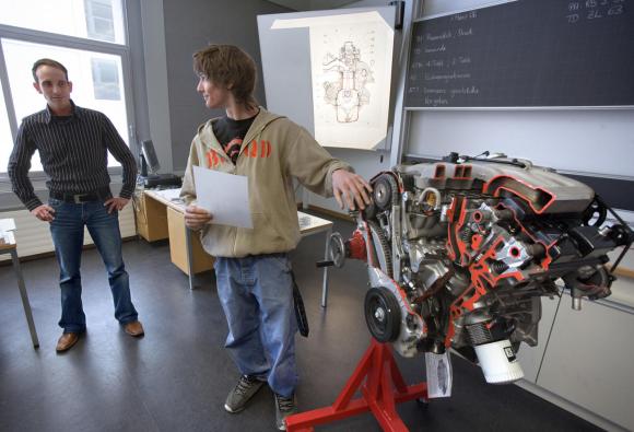 شاب ميكانيكي متدرب يقف إلى جانب محرك داخل فصل دراسي