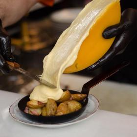 Una persona sirve queso fundido sobre un sartén con papas