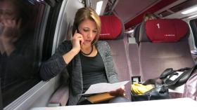 donna al telefono mentre legge un incarto, seduta in treno.