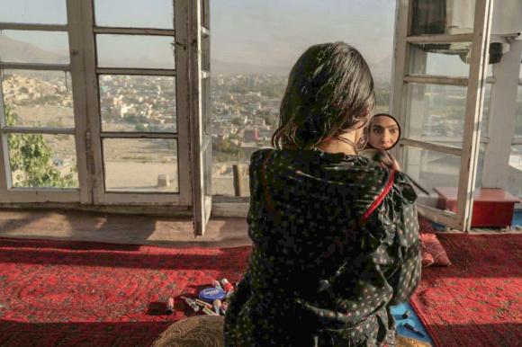 Woman sees herself on a mirror, with a city view sprawling beyond her window