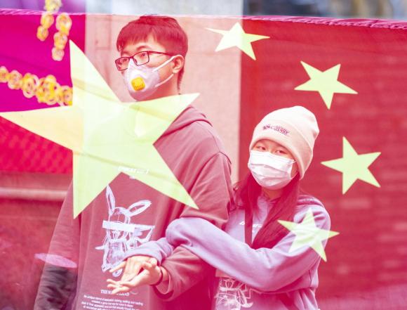 Two masked people behind Chinese flag