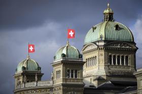 Bundeshaus mit Schweizer Fahnen unter einem dunklen Himmel.
