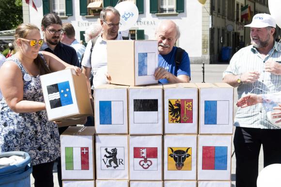 alcune persone posano delle scatole su cui ci sono gli stemmi dei cantoni svizzeri.