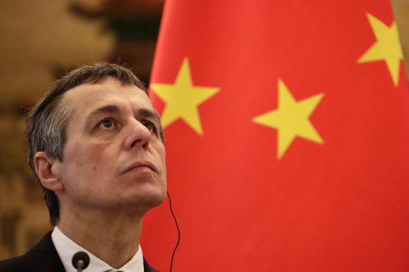 Il viso di Ignazio Cassis con lo sguardo rivolto verso l alto e sullo sfondo la bandiera della Cina.