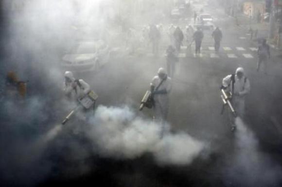 Tres hombres fumigan las calles, los rodea una espesa capa de humo