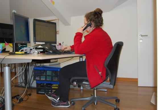 Una giovane seduta a una scrivania telefona guardando lo schermo del computer