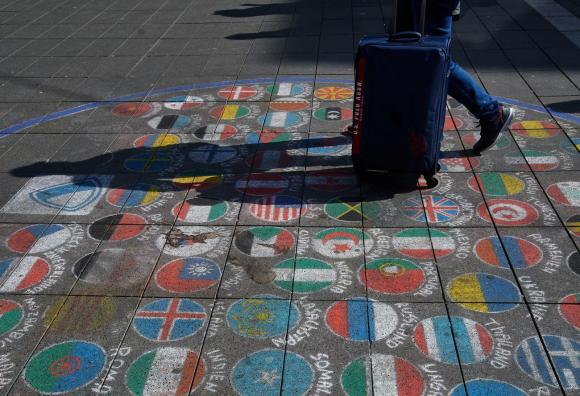 Ein Mann schiebt seinen Koffer über Flaggen verschiedenster Länder, die mit Kreide auf den Boden der Fußgängerzone gemalt wurden
