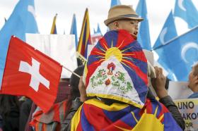 A boy sits on his father s shoulders draped in a Tibetan flag