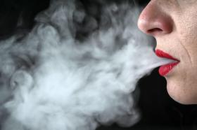 Eine Frau raucht eine E-Zigarette. Sichtbar sind nur Nase, Mund und der austretende Dampf.