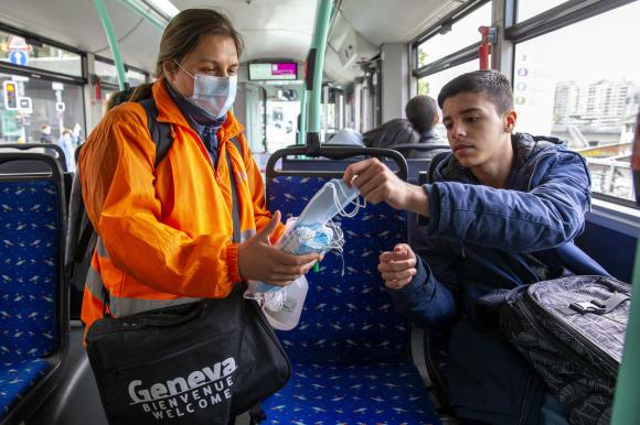 Member of staff hands out face mask to a passenger in Geneva tram