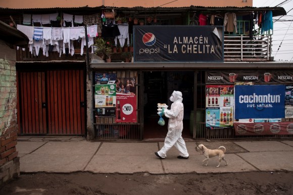 Eine Person, die eine Maske und Schutzkleidung trägt, geht mit ein paar Kisten Lebensmittel durch ein Armenviertel
