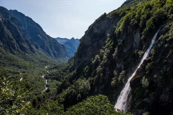 Veduta aerea di valle alpina molto incavata; vegetazione domina; cascata sulla destra.