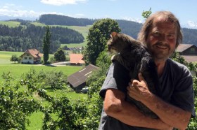 Hombre con gato, al fondo, paisaje de los Alpes
