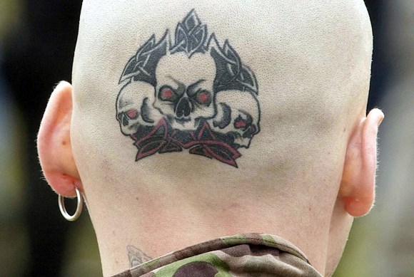 Testa di un uomo rasata su cui sono tatuati tre teschi.