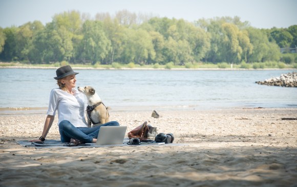 パソコンと犬と一緒に水辺に座る女性