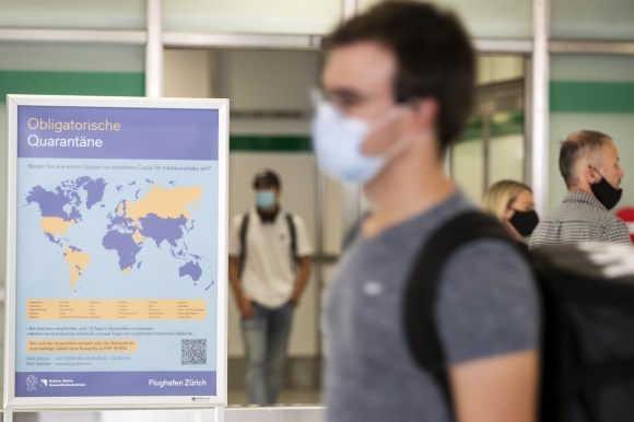 Un hombre con mascarilla observa un aviso en el aeropuerto de Zúrich