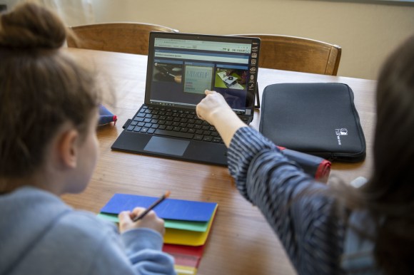 Schuelerinnen einer fuenften Klasse erhalten Aufgaben per Tablet Computer und loesen diese zuhause.
