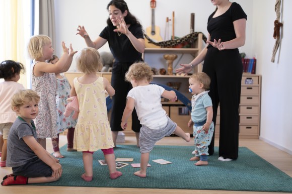 Young children dance with a woman in a childcare setting