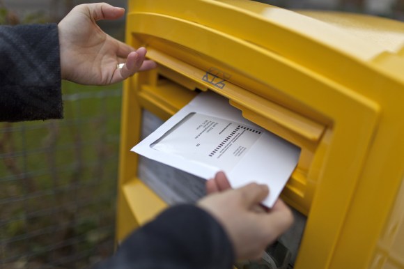 Eine Hand steckt einen Umschlag in einen Briefkasten
